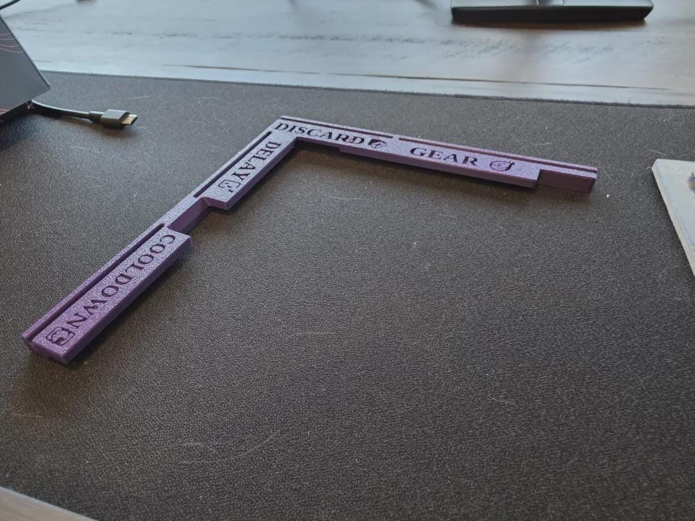 Purple 3D printed board game organizer with labeled sections for cooldown, delay, discard, gear on table.