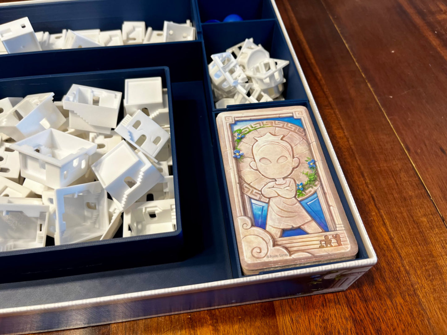 KreativLayers Santorini board game organizer with compartments for game pieces and cards, featuring a sleek design.