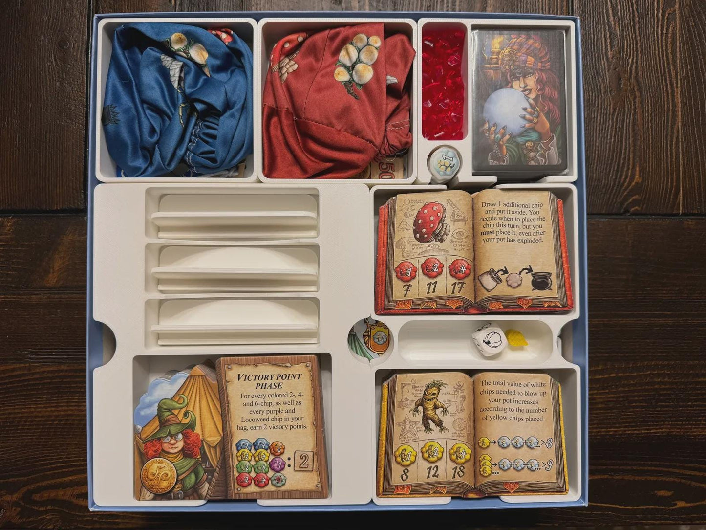 Board game organizer with compartments storing cards, tokens, and bags, featuring illustrated game pieces