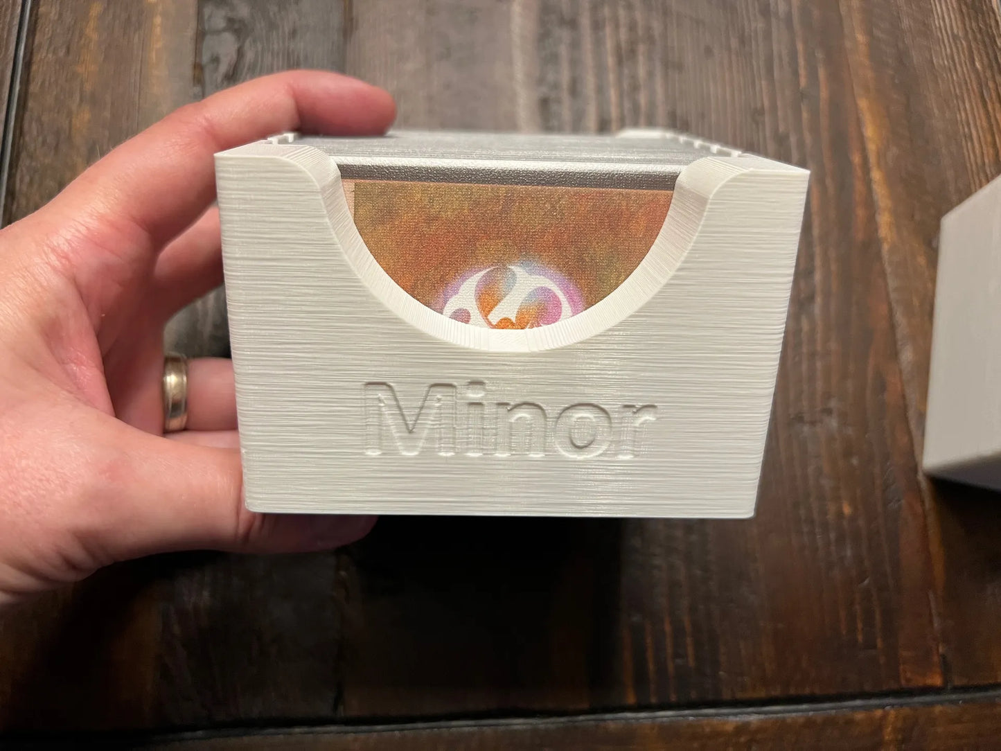 Hand holding 3D printed board game card organizer labeled 'Minor' by KreativLayers on wood table