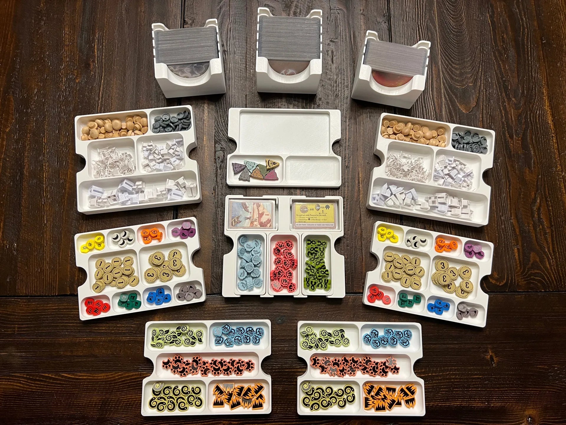 3D printed board game organizer with trays holding colorful tokens and cards on a wooden table