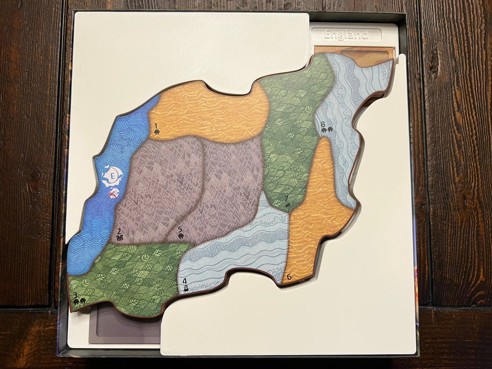 Custom 3D printed board game organizer insert holding map tile in game box on wooden table
