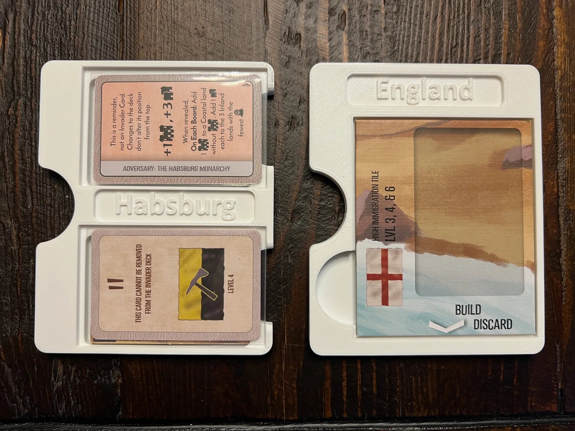 3D printed board game organizer trays labeled Habsburg and England, holding game cards on wood table.